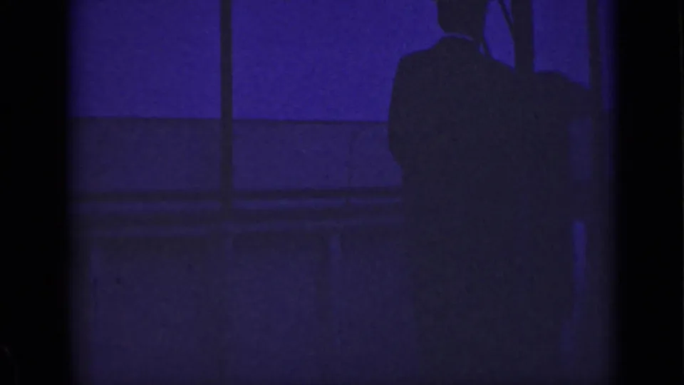 1940 Ontario 8mm frame with a nearly still male silhouette at right, seen against dark railing shapes and purple-blue exposure.