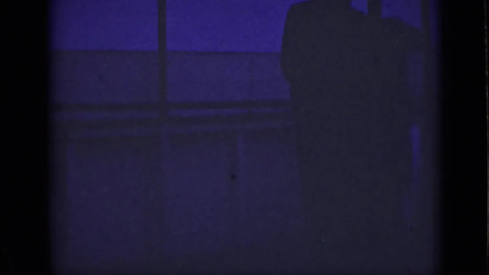 1940 Ontario 8mm frame showing the adult figure partly cropped near bridge or waterfront railings in heavy shadow.