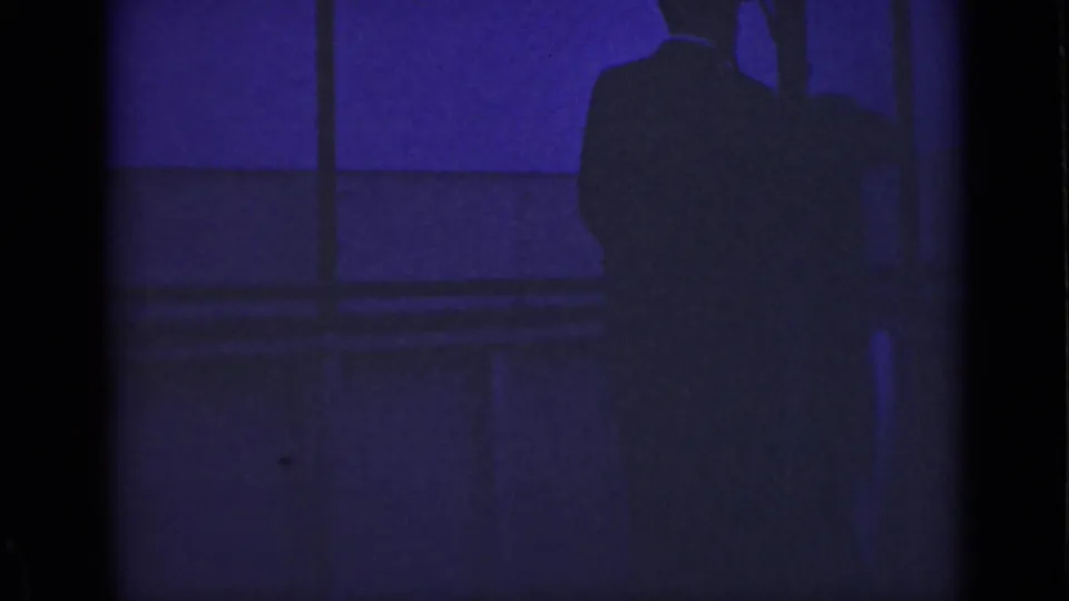 1940 Ontario 8mm frame with a backlit adult man standing near a bridge or waterfront railing in deep purple-blue light.