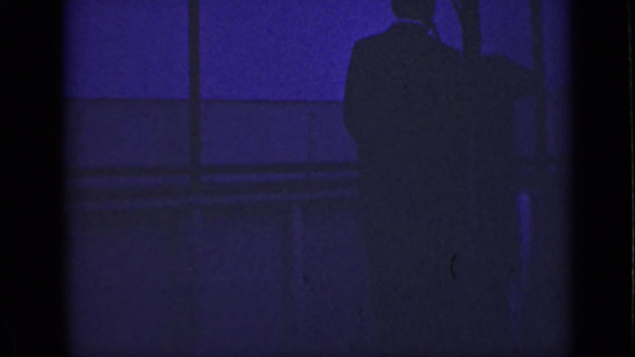 Dark silhouette of a standing man near a window in purple-blue light.