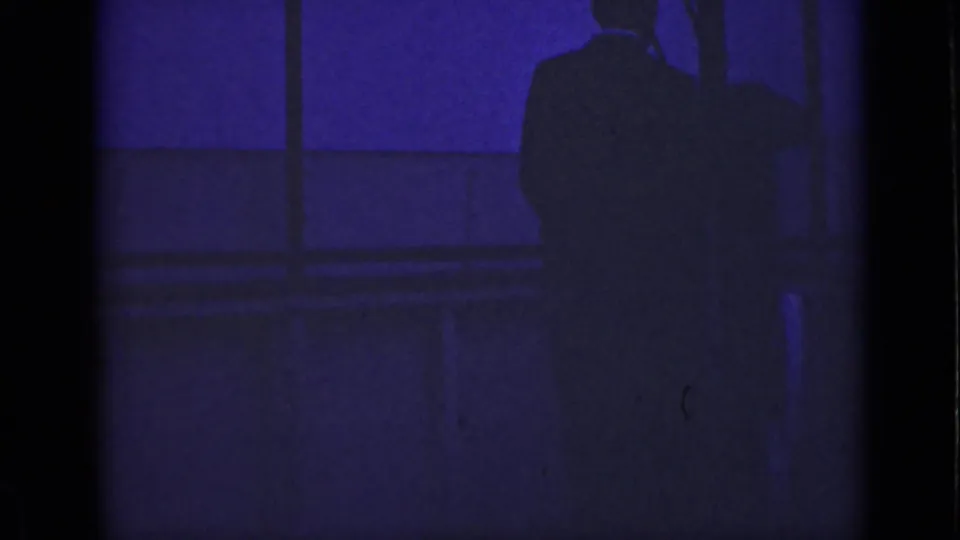 1940 Ontario 8mm frame showing a dark suited silhouette near window panes under purple-blue low light.