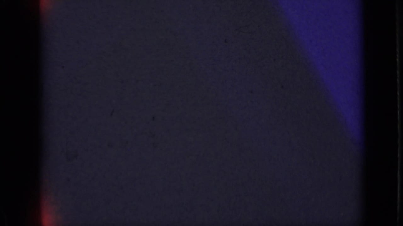 Mostly dark frame with purple-blue exposure and black film edges.