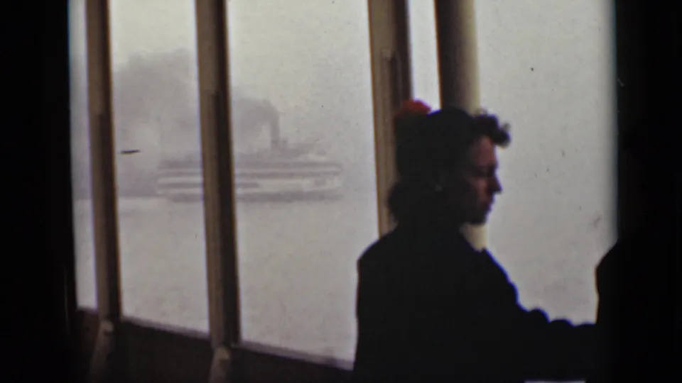 1940 Ontario home-movie frame with a silhouetted adult near window mullions as a smoky vessel moves through fog outside.