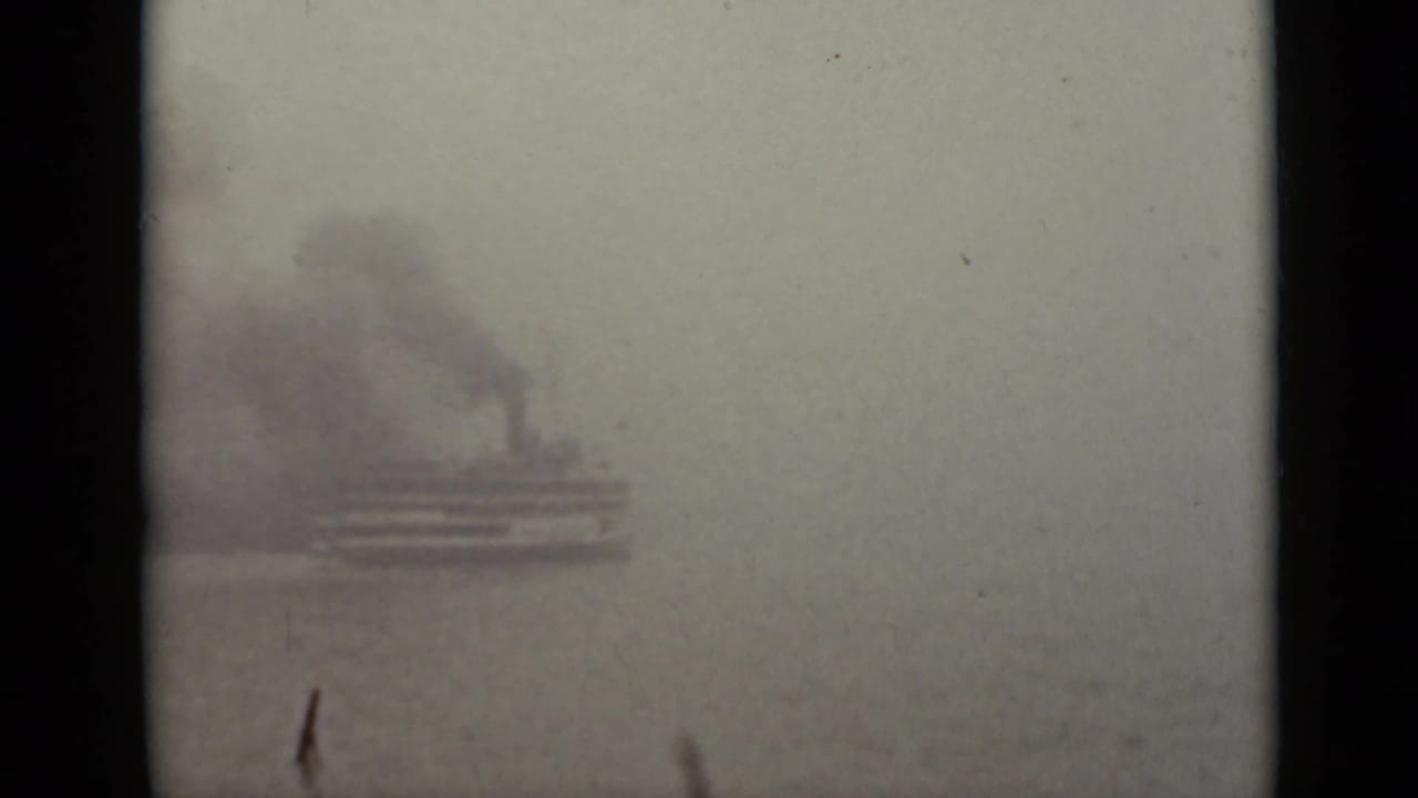 Foggy water view with a low vessel and dark smoke seen through a window.