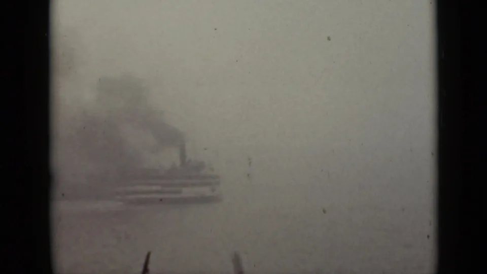 1940 Ontario 8mm frame with a blurred vessel crossing fog-covered water, framed by dark film and window edges.
