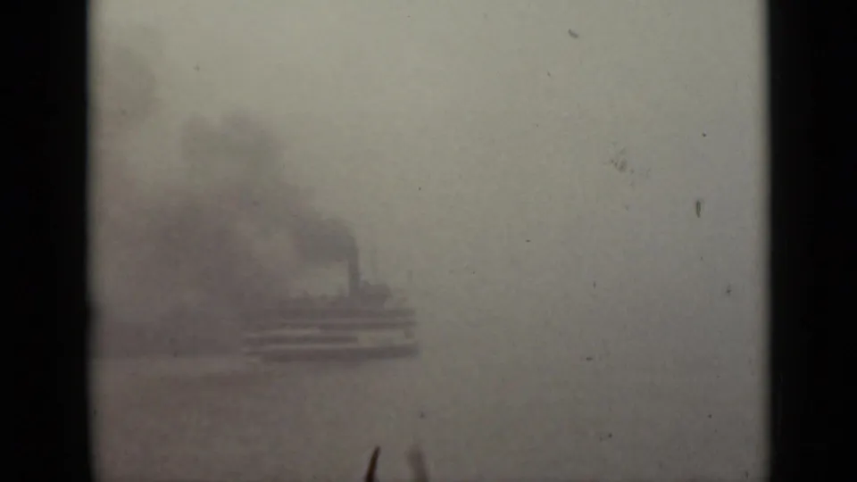 A 1940 Ontario home-movie frame shows a distant vessel and smoke plume through dense fog, with dark vertical framing at the side.