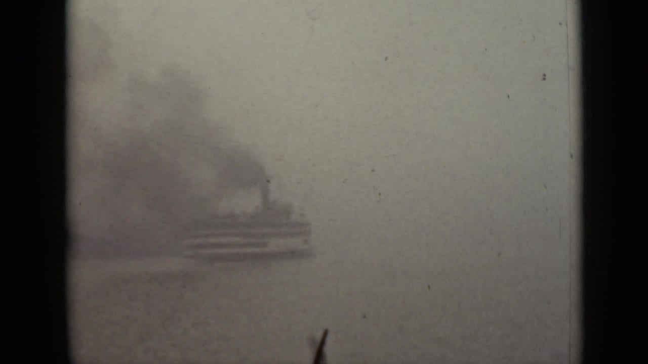 Small vessel silhouette barely visible through dense fog on calm water.
