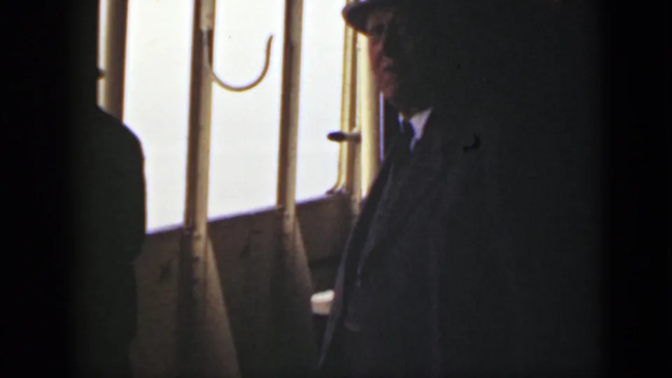 The suited passenger remains near the window, partly in shadow against the overexposed water outside the boat.