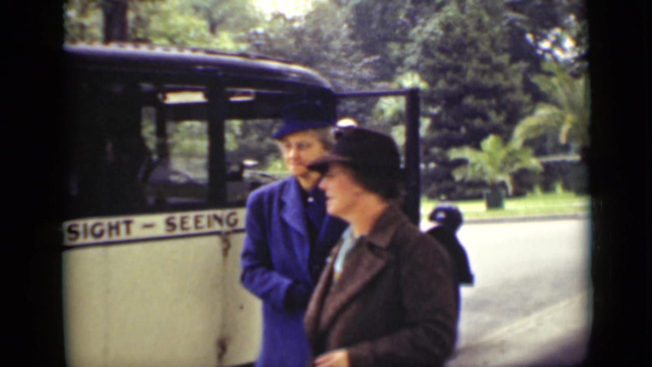 Two women in hats stand beside a bus marked SIGHT-SEEING.