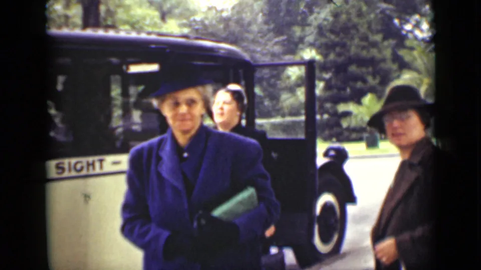 1940 Ontario home-movie frame showing women in formal coats and hats beside the sightseeing bus.