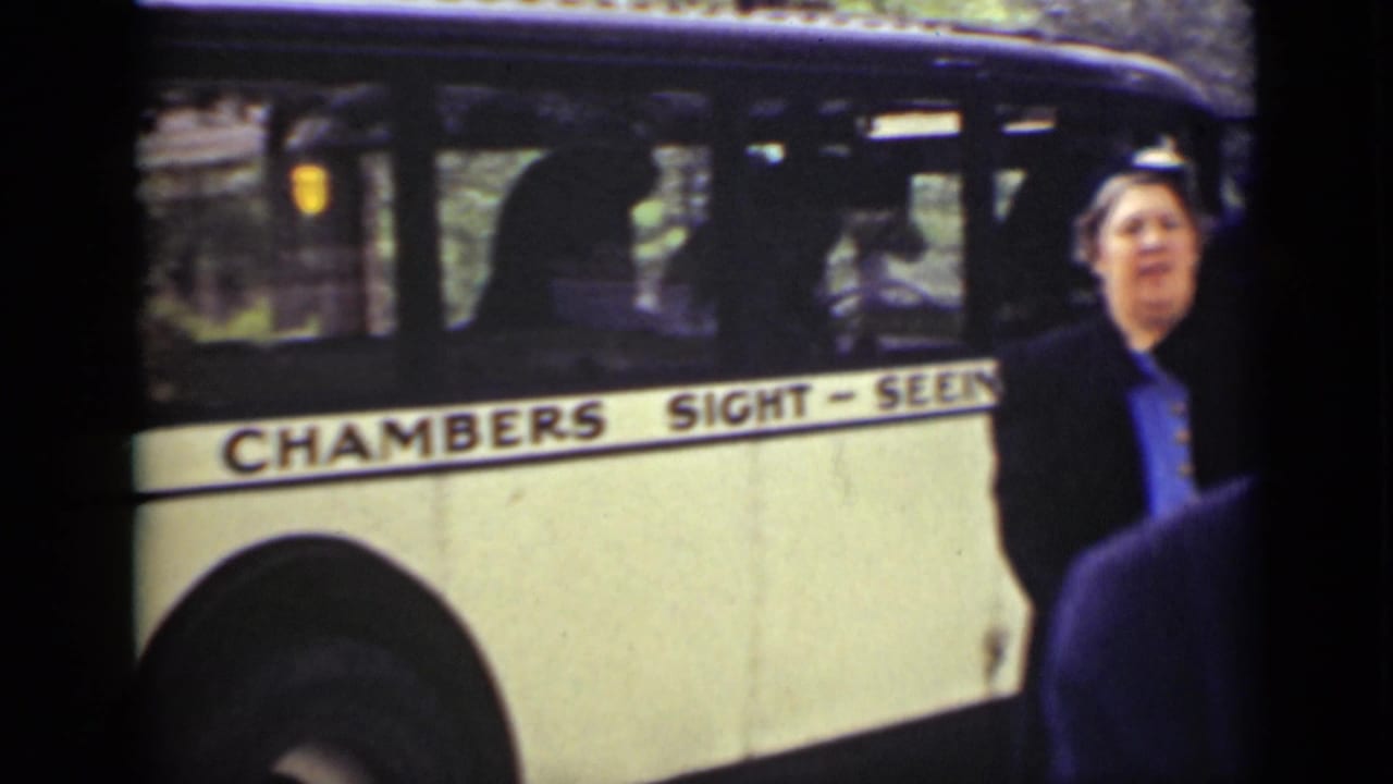 Woman in a dark coat stands beside a cream Chambers Sight-Seeing bus.