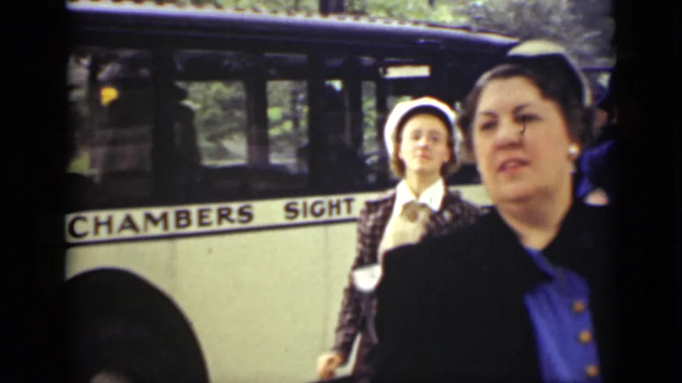 Two women in period coats and hats appear beside the Chambers Sight-Seeing bus, with one woman closer to the camera.