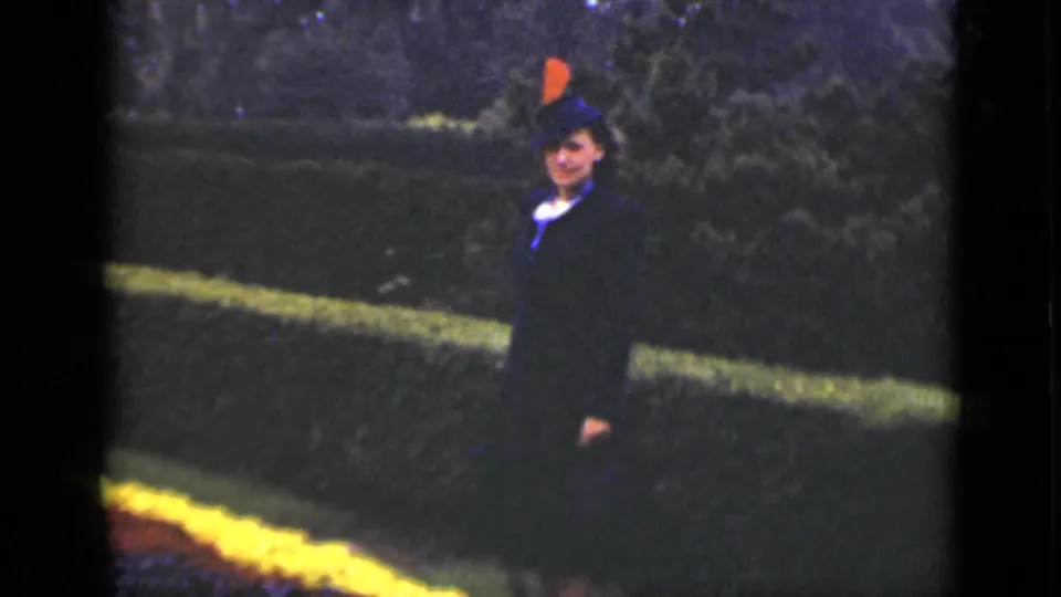 A woman in formal dark attire faces the camera in a manicured Ontario garden circa 1940, with hedges and a yellow flowerbed behind her.