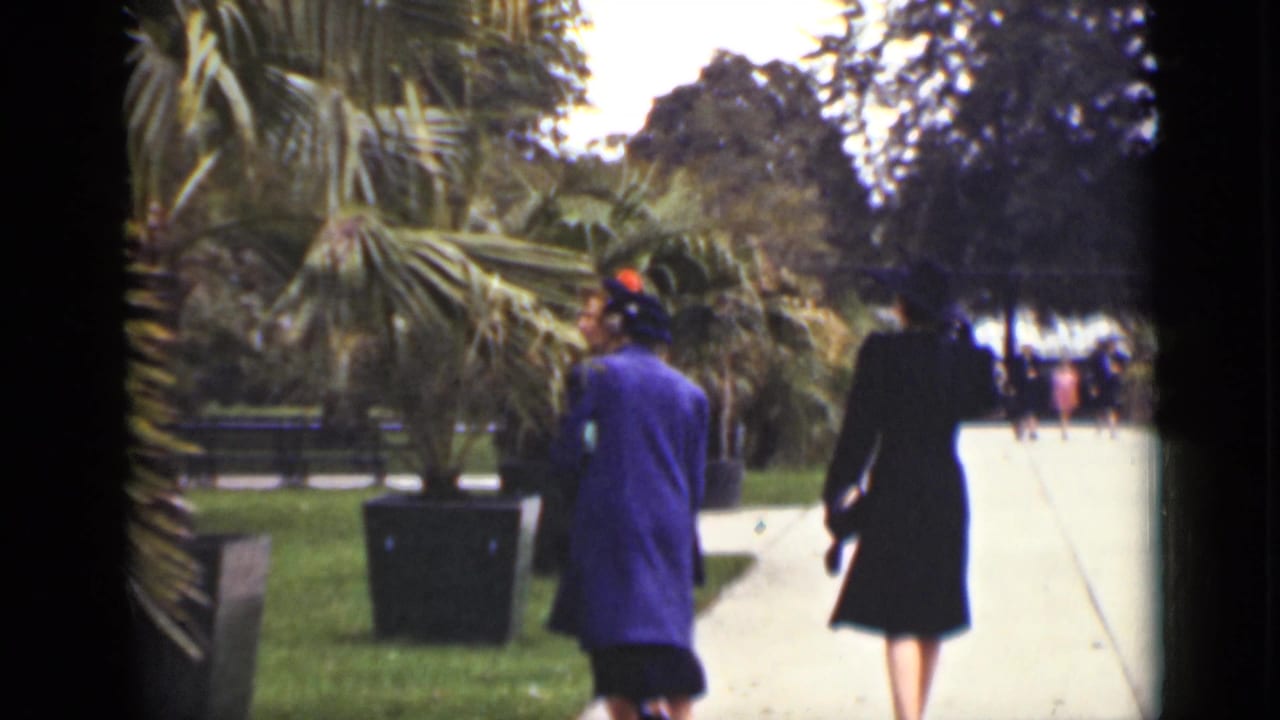 1940 Ontario home-movie frame of women in dark and blue coats walking through a landscaped public square.