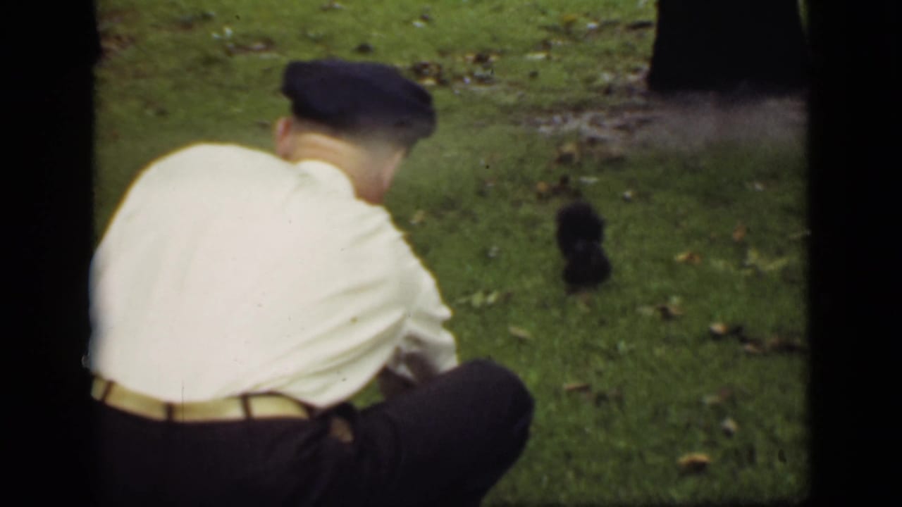 In 1940s Ontario home-movie footage, a man in a white shirt and dark cap crouches on a lawn near a small black squirrel.