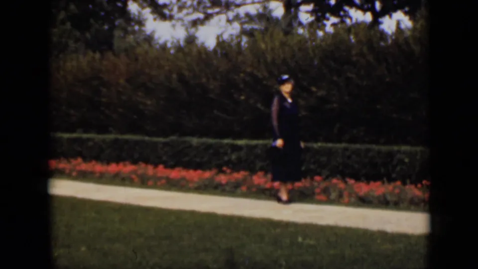A woman in a dark dress and hat stands along a garden path in metadata-supported 1940s Ontario footage.