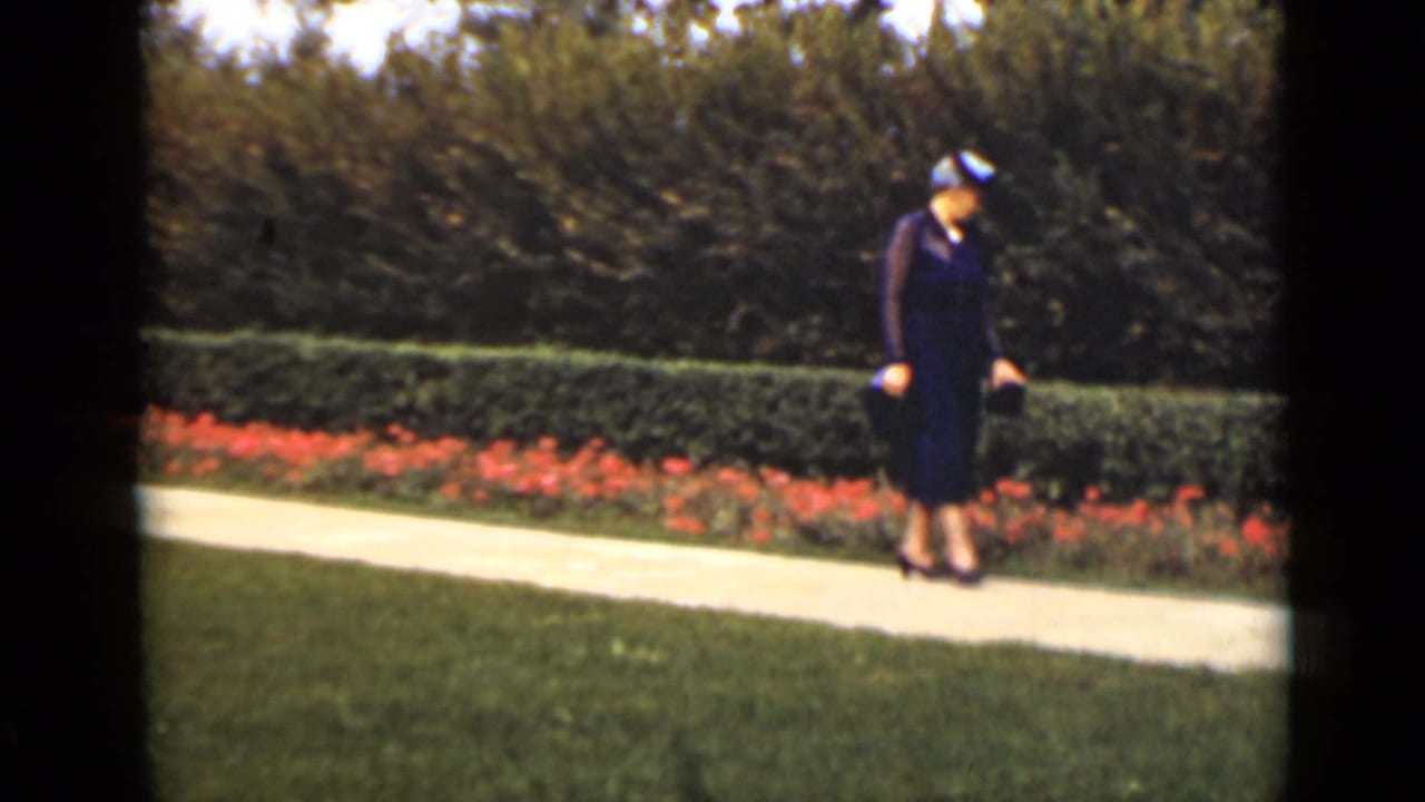 Woman in formal dress looking downward while walking on a garden path.