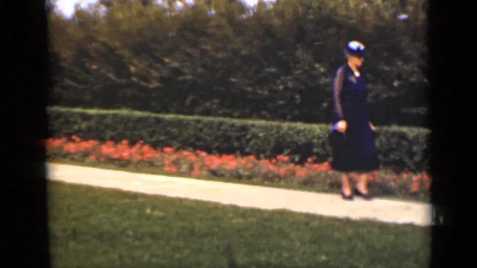 A closer 1940 Ontario frame shows the woman in a dark dress and hat walking beside the manicured garden border.