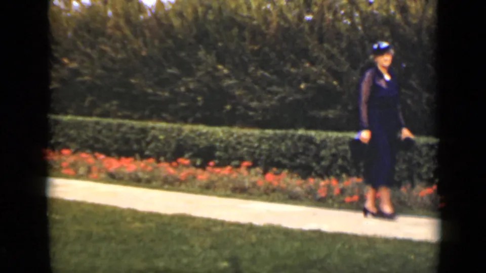At the end of the clip, the woman appears near the right side of the 1940 Ontario garden path, framed by flowers and hedges.