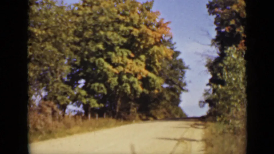 1940 Ontario home-movie still showing forward travel along a tree-bordered rural road.
