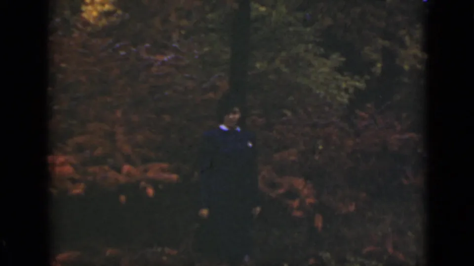 Adult woman in dark clothing with a pale collar stands among reddish autumn foliage in Ontario home-movie footage from 1940.