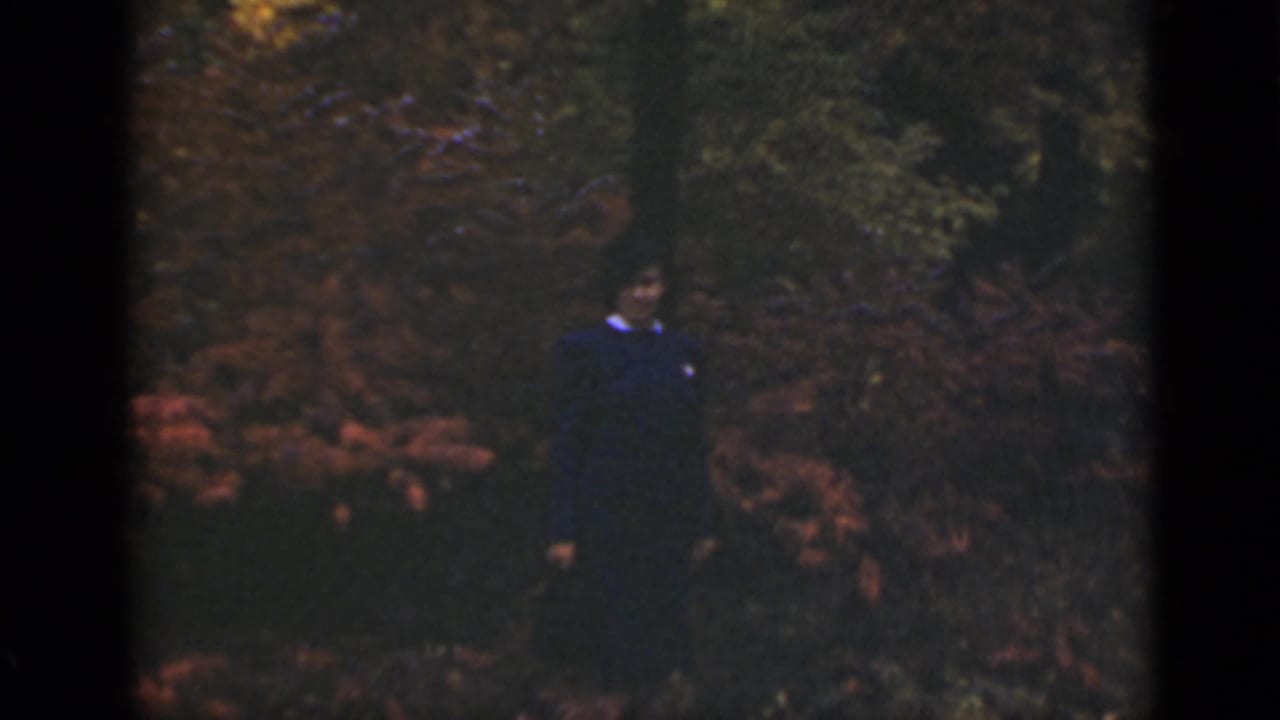 Woman standing in front of dense reddish foliage and trees.