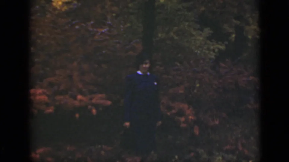 The woman remains posed in a wooded Ontario setting, framed by autumn foliage and soft 8mm color.