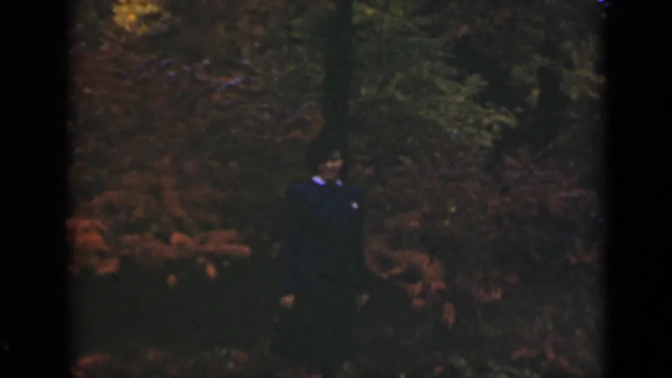 A soft 8mm frame shows the woman lower in the composition, surrounded by dark woods and reddish autumn plants.