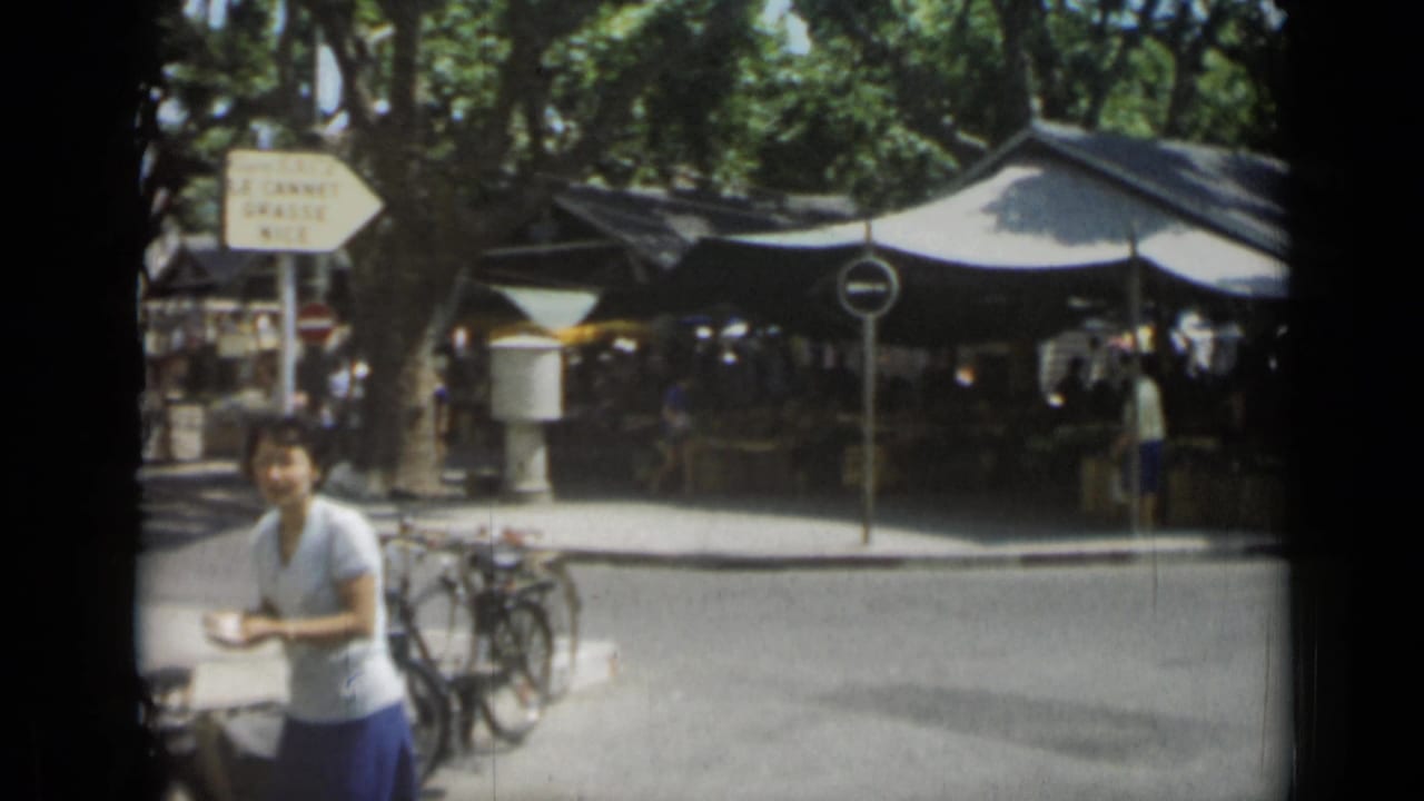 Man crossing in front of a shaded outdoor market with bicycles and street signs nearby.
