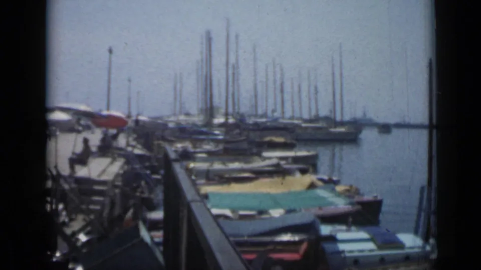 The Cannes waterfront remains in view, with moored boats in the foreground, sailboat masts across the harbor, and people along the pier.