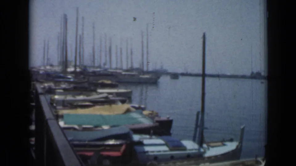1962 Cannes marina scene showing moored boats with fabric covers, dense sailboat masts, calm water, and a dark vertical frame edge.