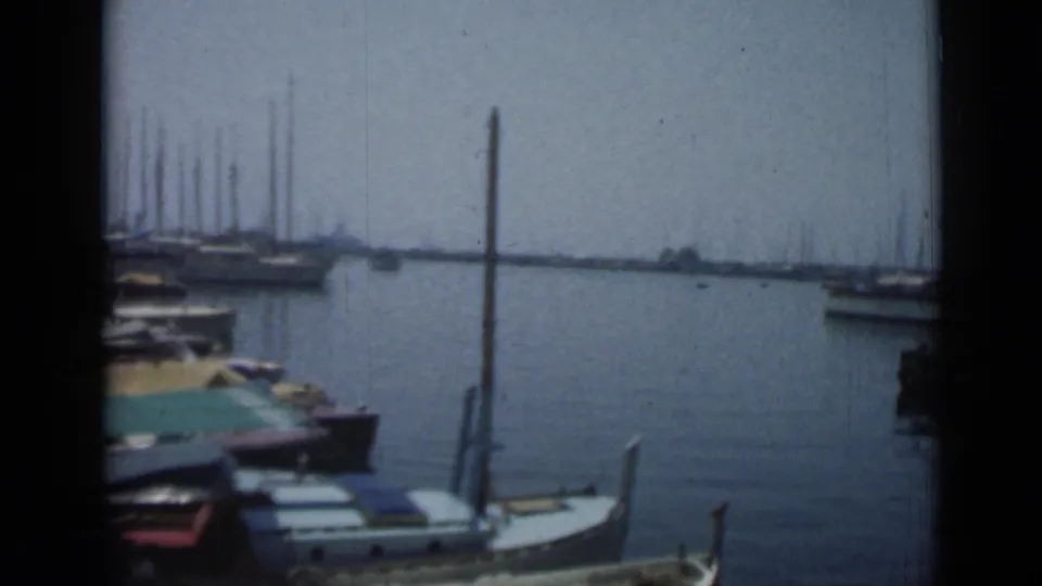 1962 Cannes harbor frame with a small covered boat by the dock, a tall post, distant sailboats, calm water, and dark 8mm frame borders.