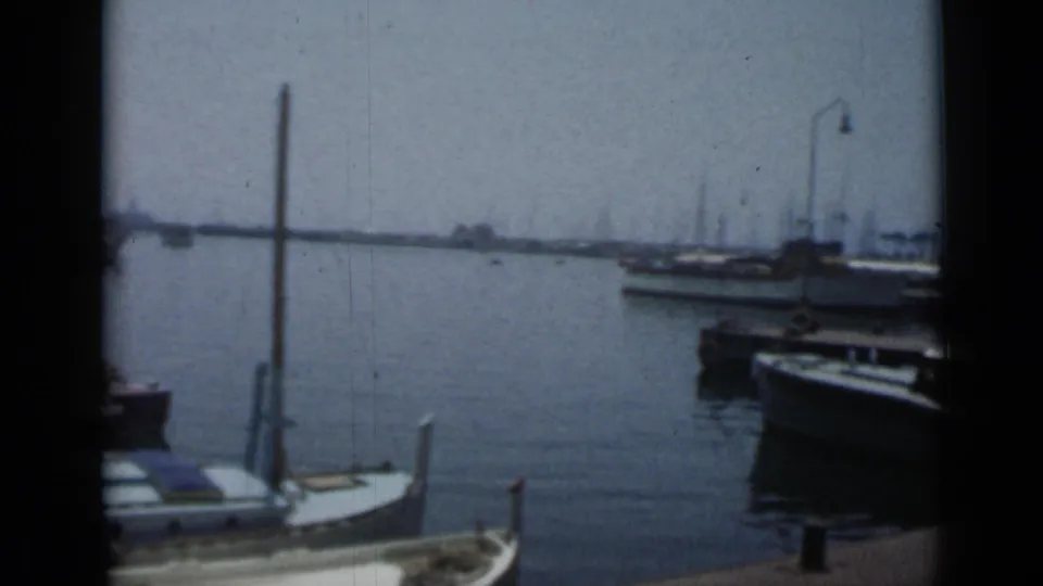 Cannes harbor in 1962 showing docked boats, calm blue water, a vertical mooring post, and curved quay lamps near the waterfront.