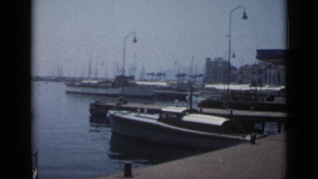Small boats moored beside a pier with harbor lamps and distant waterfront buildings.