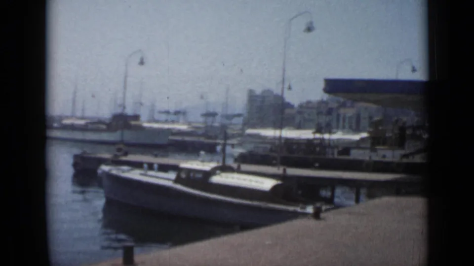 1962 Cannes harbor scene showing docked leisure craft, pier lamps, calm water, and waterfront buildings in faded 8mm footage.