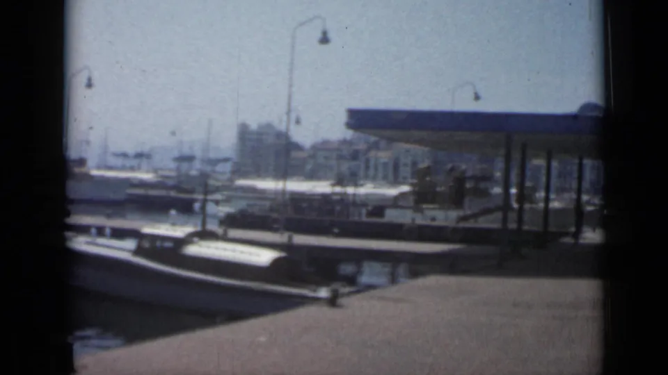 1962 Cannes pier view with moored boats, a covered dock structure, harbor masts, and distant waterfront buildings.