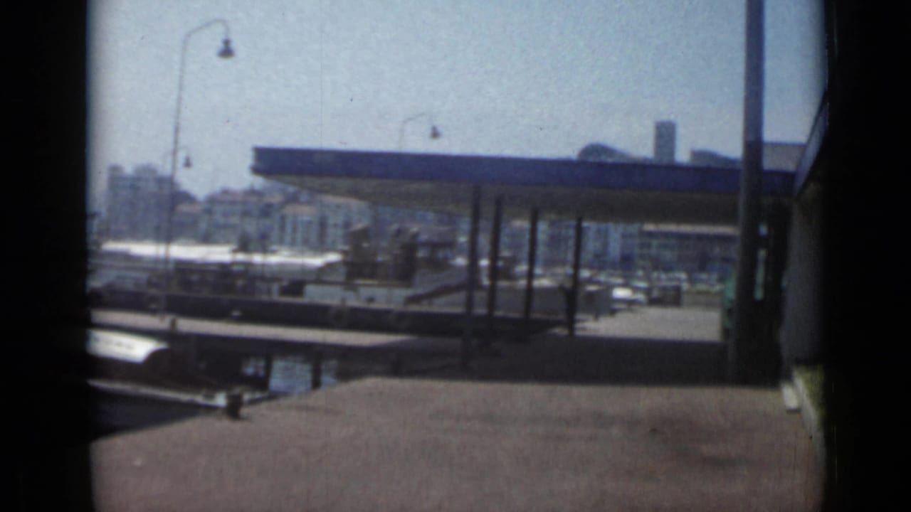 Harbor dock with a blue-roofed shelter, moored boats, and waterfront buildings beyond.