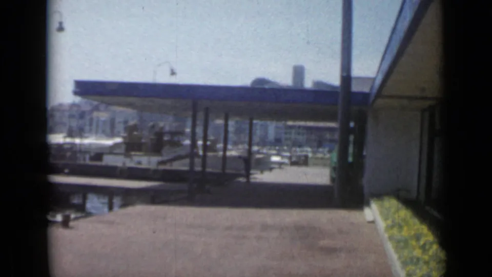 Cannes harbor scene from 1962 showing a blue-roofed dock structure, moored boats, and Mediterranean waterfront buildings.