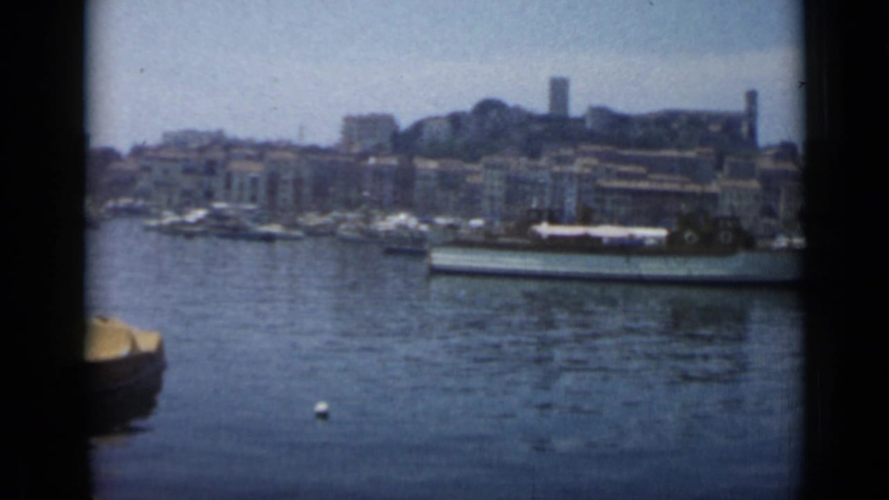 Harbor water with small boats, waterfront buildings, and a tower on a hillside beyond Cannes.