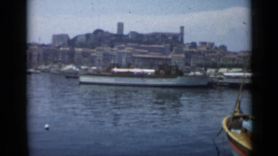 1962 visitor-shot Cannes harbor view with waterfront buildings, moored boats, buoy, and a nearby boat entering the lower edge.