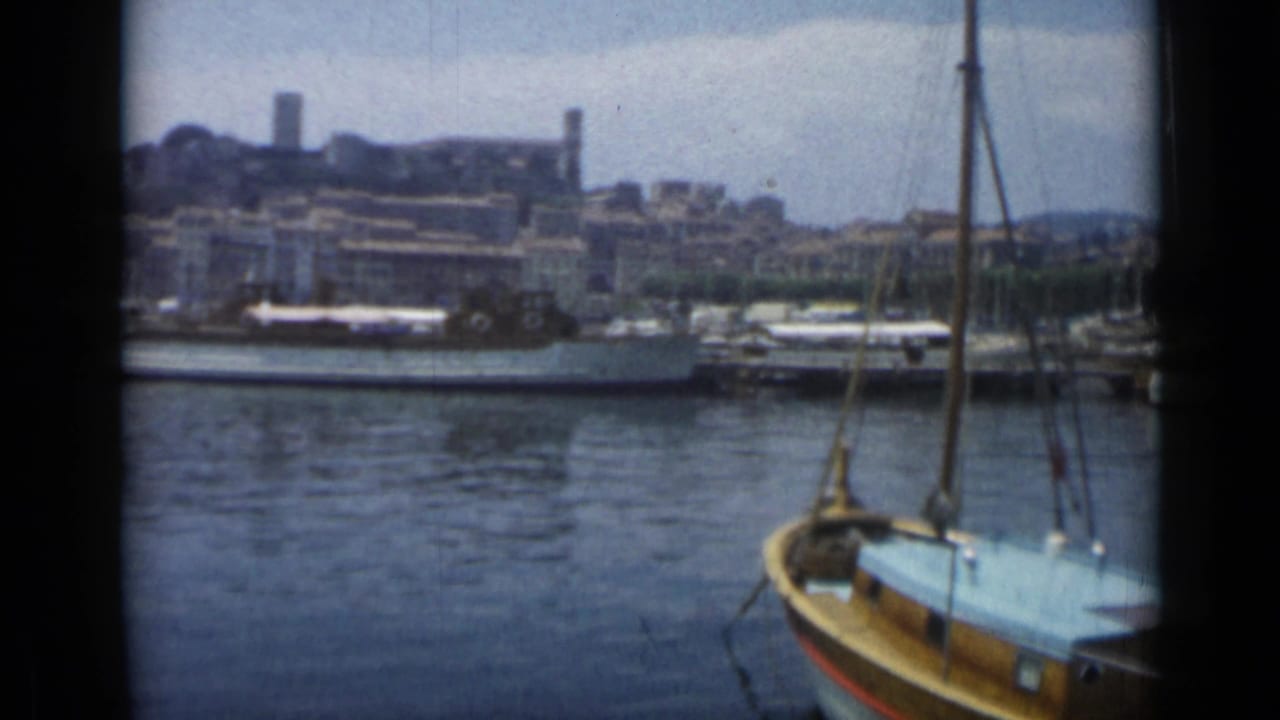 Harbor water with a wooden sailboat in front and docked boats across the quay.