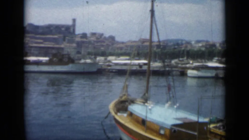 Cannes harbor in 1962, showing a sailboat bow and rigging before larger moored vessels and hillside architecture.
