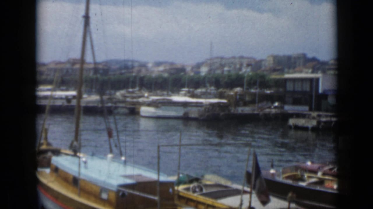 Moored boats along a sunny marina with hillside buildings in the background.