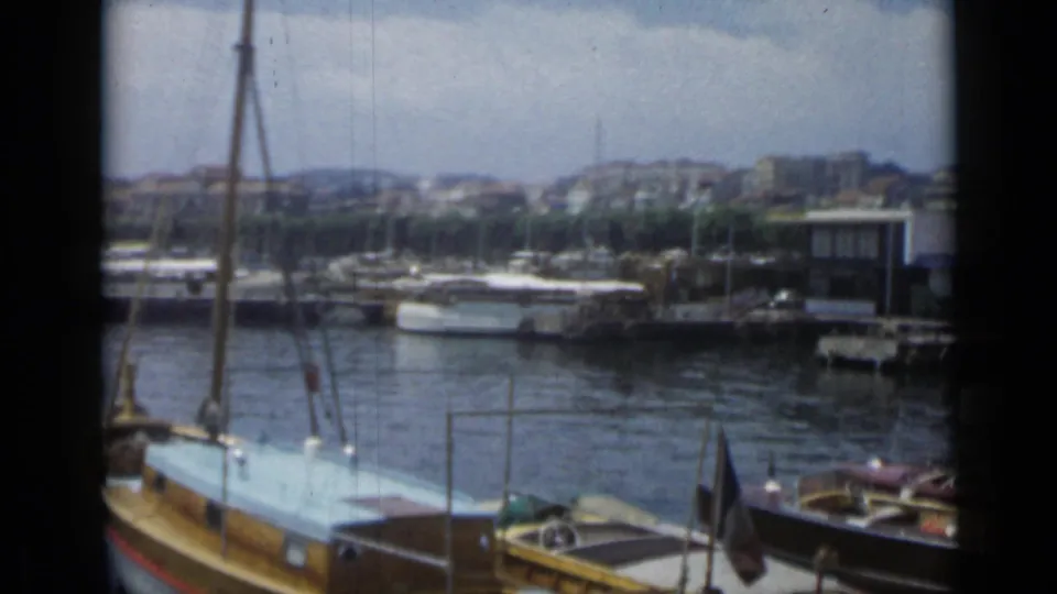 1962 Cannes marina view with docked boats, waterfront water, a French flag, and hillside buildings beyond the harbor.