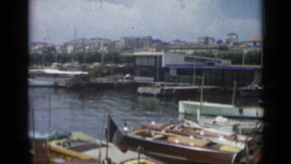 A 1962 Cannes waterfront view shows small boats, a marina structure, calm harbor water, and hillside buildings beyond the quay.