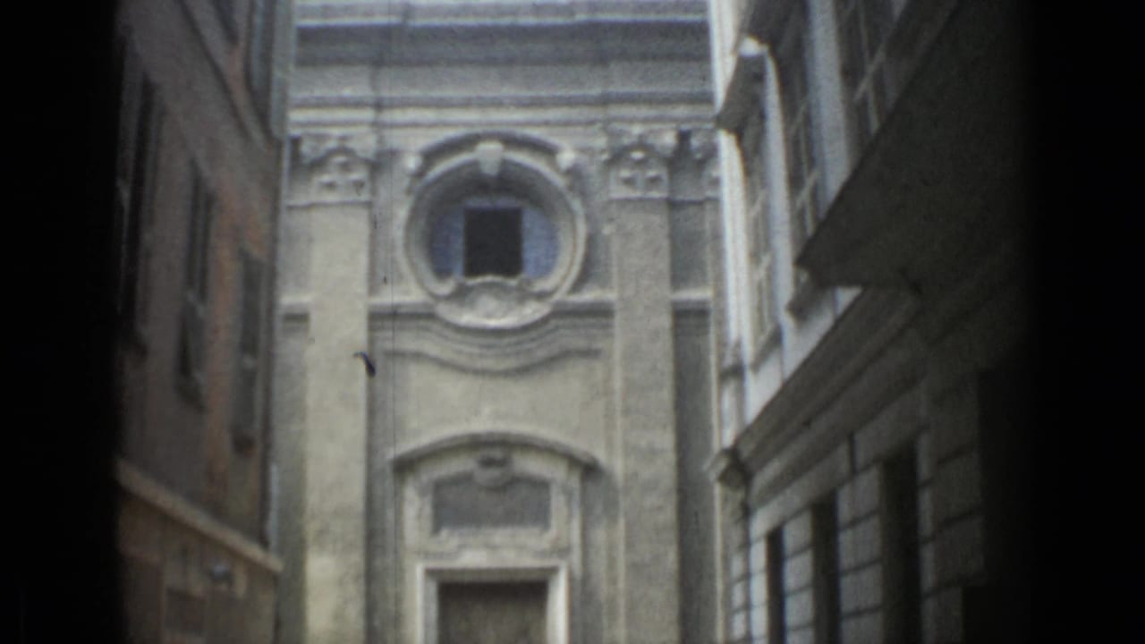 Narrow alley view toward a pale stone facade with an oculus window and doorway below.