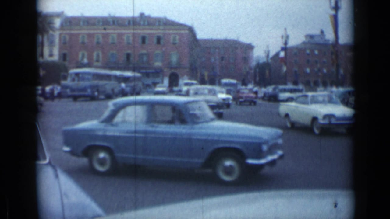 Blue sedan crossing a busy intersection with buses and cars in the background.