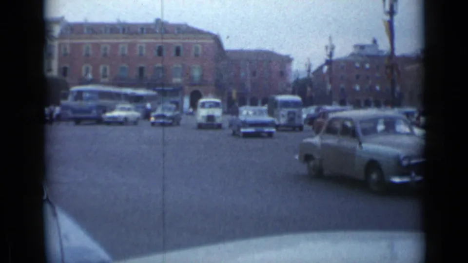 Cannes, France 1962 intersection with period cars, buses, distant pedestrians, and a large brick building.