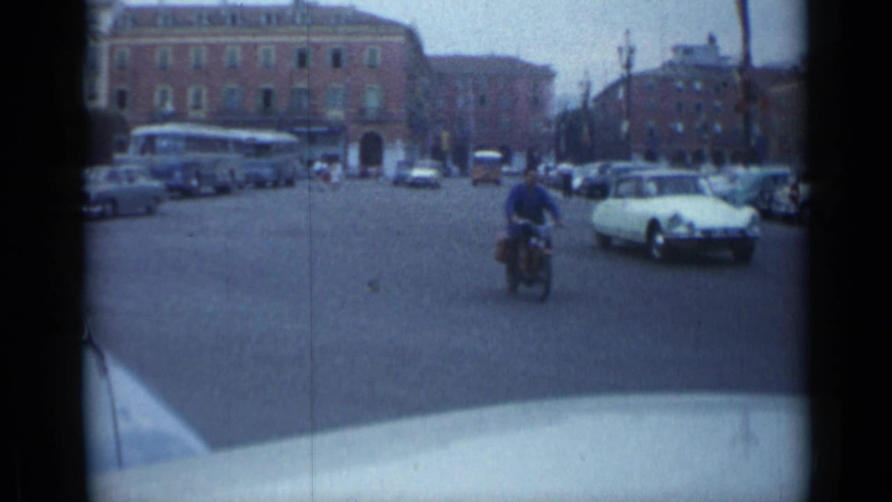 Motorcycle or scooter rider passes through a broad intersection with cars and a bus nearby.