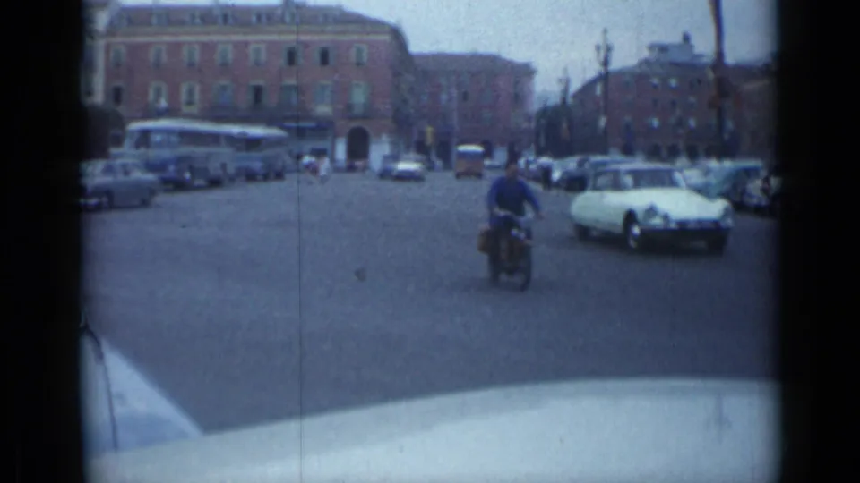 A rider crosses the 1962 Cannes intersection as cars and a bus move or wait along the street edges.